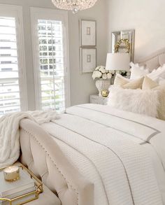 a bedroom with white bedding and gold accents on the headboard, chandelier and windows