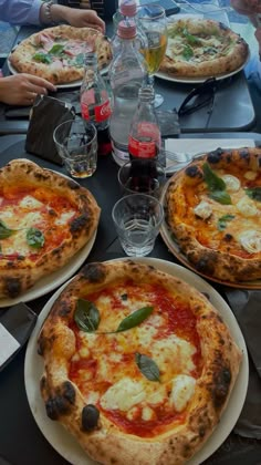 three pizzas on plates sitting on a table next to bottles of water and glasses