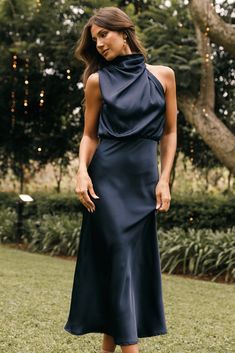 a woman standing in the grass wearing a black dress with a halter neckline