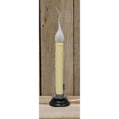 a white candle with a black base on a wooden table in front of a fence