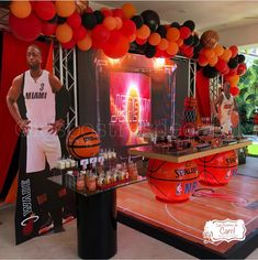 a man standing next to a basketball on top of a wooden table covered in orange and black balloons