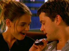 a man and woman sitting next to each other while eating food from a plate in front of them