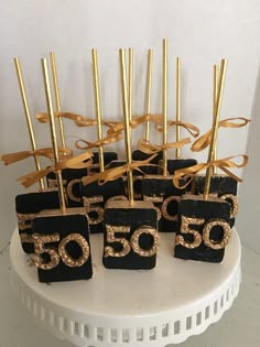 black and gold 50th birthday cake pops with golden numbers on them, tied with ribbons