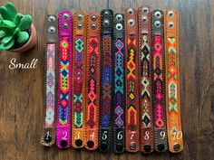 four different colored leather bracelets with numbers on them and a potted plant in the background