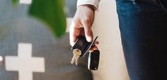 a man is holding two keys in his hand while standing next to another person's purse