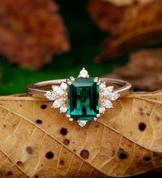 an emerald colored stone surrounded by white diamonds sits on top of a leaf in the grass