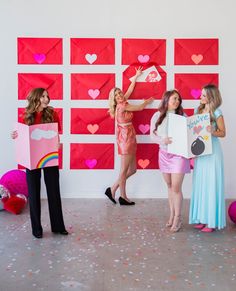 three girls holding up valentine's day cards in front of a wall with hearts