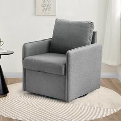 a gray chair sitting on top of a wooden floor next to a table and lamp