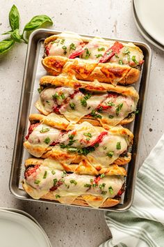 a pan filled with lasagna shells covered in cheese and sauce, garnished with fresh basil