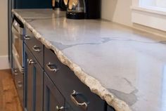 a kitchen counter with marble top and metal handles on the bottom drawer, in front of an oven