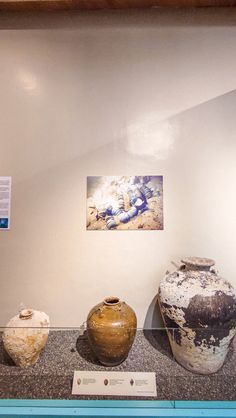 three vases sitting on display in a glass case next to a wall with pictures