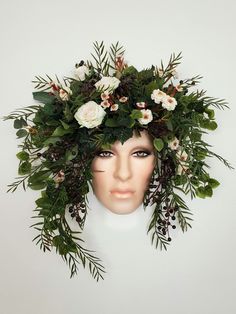 a mannequin head with flowers and greenery on it's face, against a white background