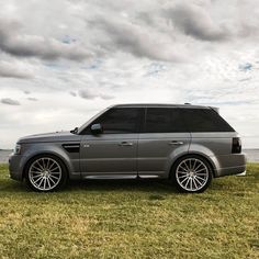 a grey range rover parked on the grass by the water with clouds in the background