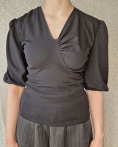 This unbranded black wool jersey top has gathered details at the centre front neck, shoulders and cuffs. A slim fit with elbow-length sleeves and V-neckline. All seams are overlocked and finished with eyelet lace. This was a designer sample, so is the only one of its kind. Good used condition with no pulls, tears, stains or damage. Black Gathered Sleeves Top For Evening, Black Evening Tops With Gathered Sleeves, Black Evening Top With Gathered Sleeves, Fitted Tops With Asymmetrical Zipper Closure, Asymmetrical Black Top With Buttons, Asymmetrical Neckline Top With Ruched Detail, Black Asymmetrical Cotton Top, Issey Miyake Pleats Please Top, London Fashion Week Mens