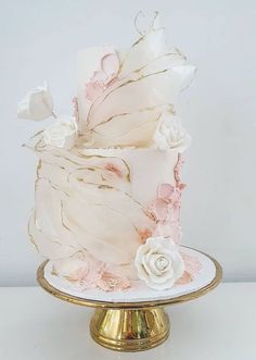 a white and pink wedding cake on a gold plate with flowers in the frosting