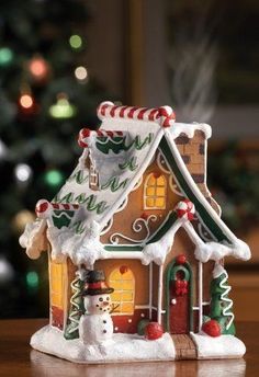 a small christmas house on a table with a tree in the background