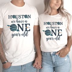 two people wearing t - shirts that say houston we have a one year old and the other