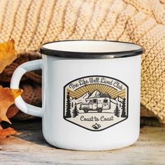 a camper mug sitting on top of a wooden table next to an autumn leaf