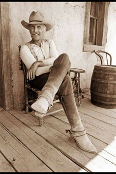 an old photo of a man sitting on a porch wearing cowboy boots and a hat