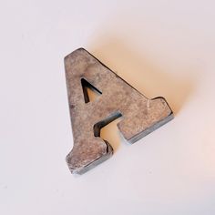 the letter a is made out of metal and sits on a white surface with a shadow