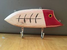 a red and white fish shaped object sitting on top of a hard wood floor next to a gray wall