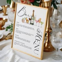 a sign that is sitting on top of a table with wine glasses and flowers in the background