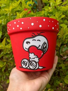 a hand holding a red pot with a cartoon character painted on the side and white dots around it