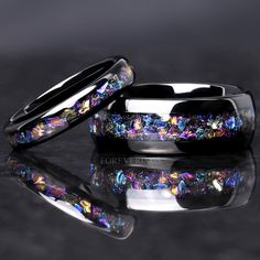 two wedding bands with multicolored opal inlays are shown on a reflective surface