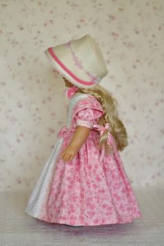 a doll wearing a pink dress and white hat with flowers on the wall behind her