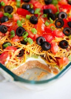 a casserole dish with black olives, tomatoes and cheese