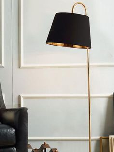 a floor lamp with a black shade on it next to a chair and bookcase