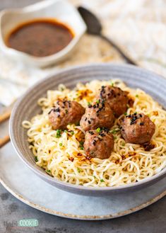 a bowl filled with noodles and meatballs next to a cup of sauce on the side