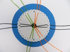 a white clock with orange and green wires connected to it on a blue circular surface