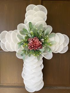 a cross decorated with flowers and greenery hangs on the front door's wooden paneling