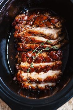 sliced pork in a slow cooker with sauce and herbs