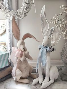 two stuffed rabbits sitting next to each other on a table near a mirror and clock