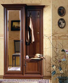 a large wooden closet sitting next to a vase filled with flowers and a mirror on the wall