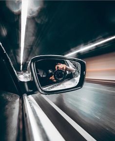 a person taking a photo in the side view mirror of a car driving through a tunnel