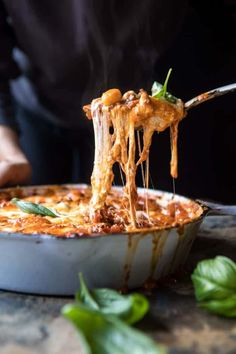 a person is taking a slice of pizza out of the casserole dish with a fork