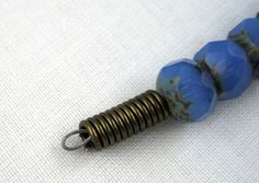 a blue beaded necklace with metal spirals on white fabric background, closeup