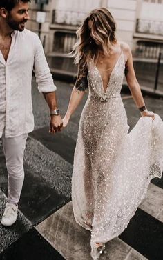 a man and woman walking down the street holding hands, dressed in all white outfits