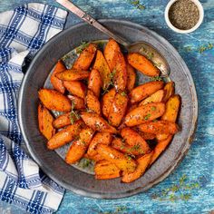 a plate full of cooked carrots on a blue tablecloth next to a spoon