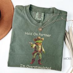 Hold on Partner, I'm Overstimulated Funny Frog Shirt, Cowboy Frog Tee, Unisex Ironic Shirt, Weirdcore Shirt. DETAILS .: Comfort Colors® Unisex Garment-dyed t-shirt. .: Made 100% with ring-spun cotton.  .: The soft-washed, garment-dyed fabric brings extra coziness to your wardrobe while the      relaxed fit makes it an excellent daily choice.  .: The double-needle stitching throughout the tee makes it highly durable while the lack     of side-seams helps the shirt retain its tubular shape. .: Direct To Garment Print, which means the dye does not sit on top like vinyl but is     embedded into the fabric. SIZING .: Please refer to our size chart for specifications. This shirt is designed to have a relaxed     fit. For a more fitted look, consider ordering a size down. For a more relaxed or Ironic Tshirt, Frog Meme, Funny Frogs, Iron Shirt, Gen Z, Comfort Color, Look Plus, Oversized Shirt, Dye T Shirt