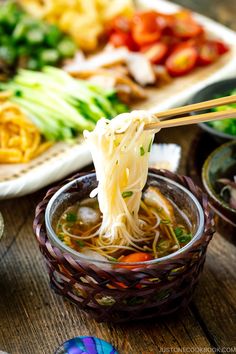 chopsticks holding noodles over a bowl of soup with vegetables and meat in the background