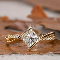 a gold ring with a princess cut diamond in the center on top of a leaf