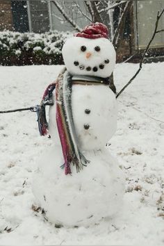 a snowman wearing a red hat and scarf standing in front of a house covered in snow