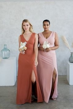 two women standing next to each other in dresses with flowers on the floor and vases behind them