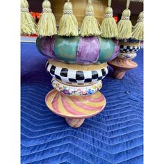 three colorful vases with tassels on them sitting on a blue table cloth