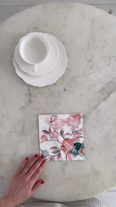 a woman's hand on a piece of paper next to a cup and saucer