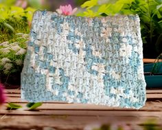 a blue and white crocheted blanket sitting on top of a wooden table next to potted plants